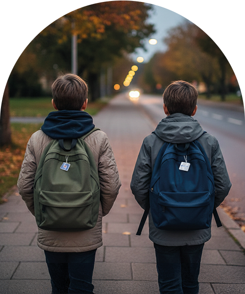 Två pojkar sedda bakifrån går på en trottoar i skymningen med ryggsäckar, varav båda har en liten reflex.